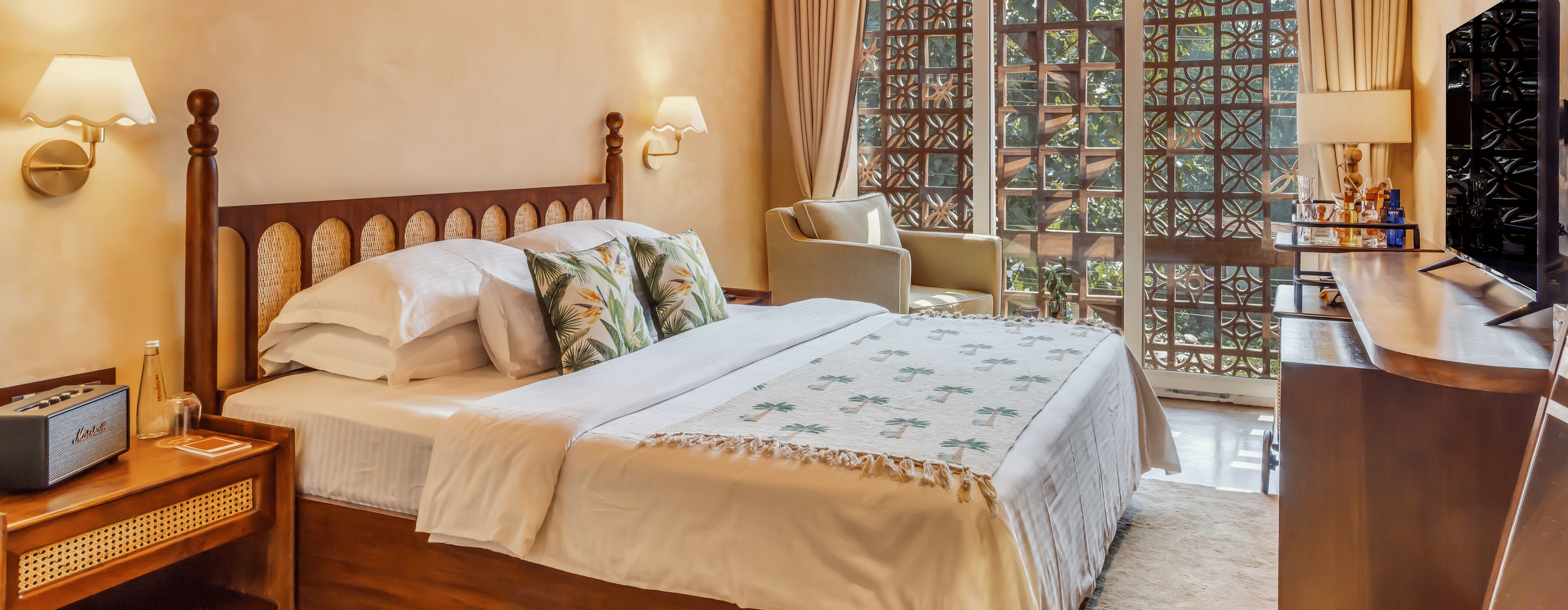 Bedroom at Unseen Boutique Hotel with wooden bed, white and green bedding, bedside lamps, window with curtains, and ceiling light fixture.
