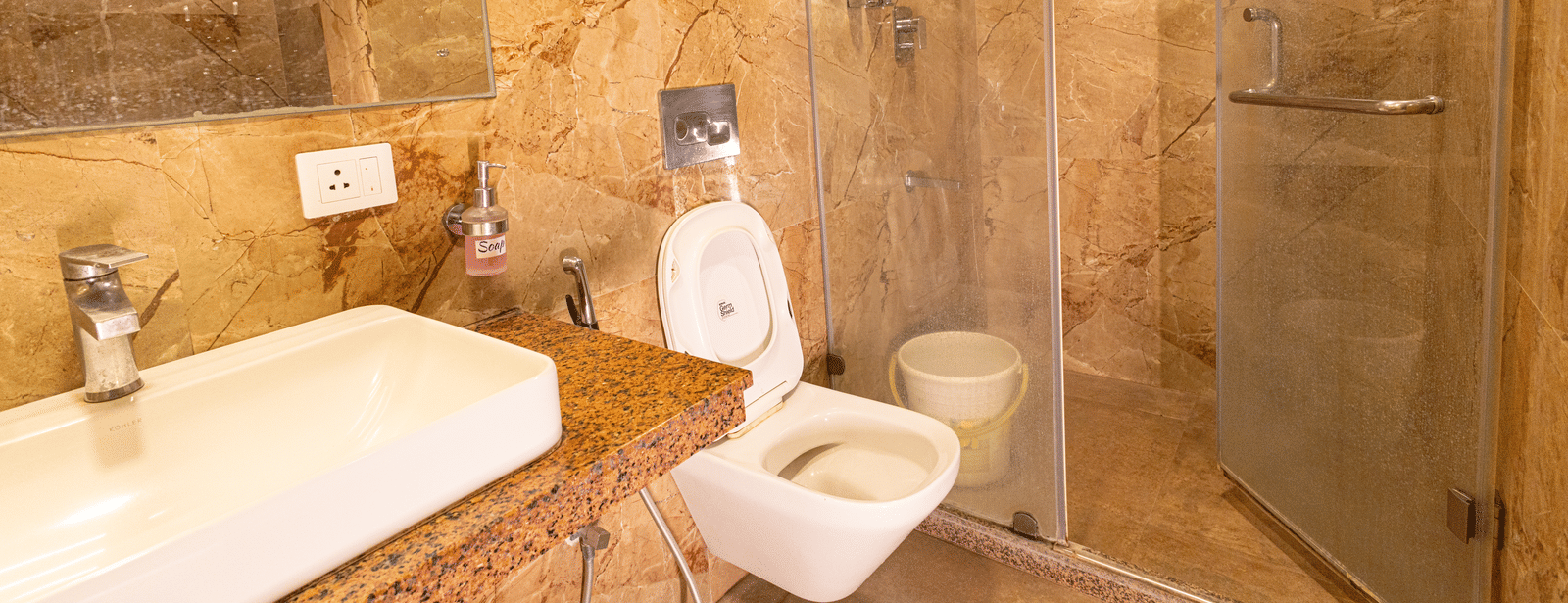A bathroom with a sink, mirror, toilet, and glass-enclosed shower area at Hotel Seagull Digha.