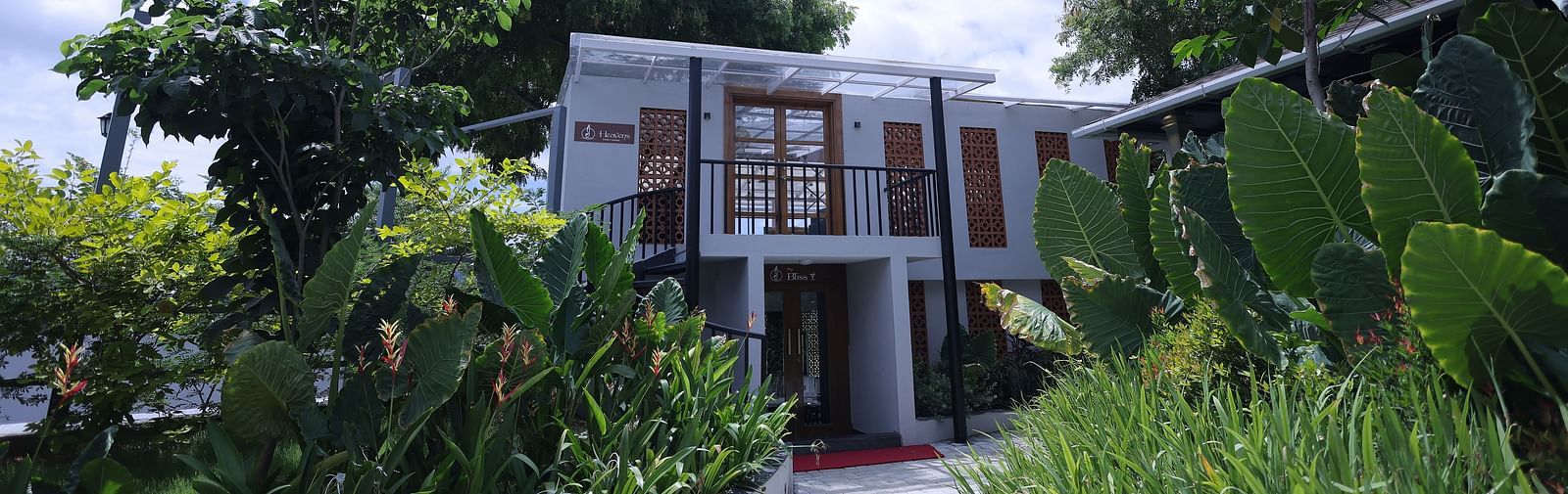 Exterior view of a villa surrounded by lush plants and trees at Trishvam Symphony, Krishnagiri.