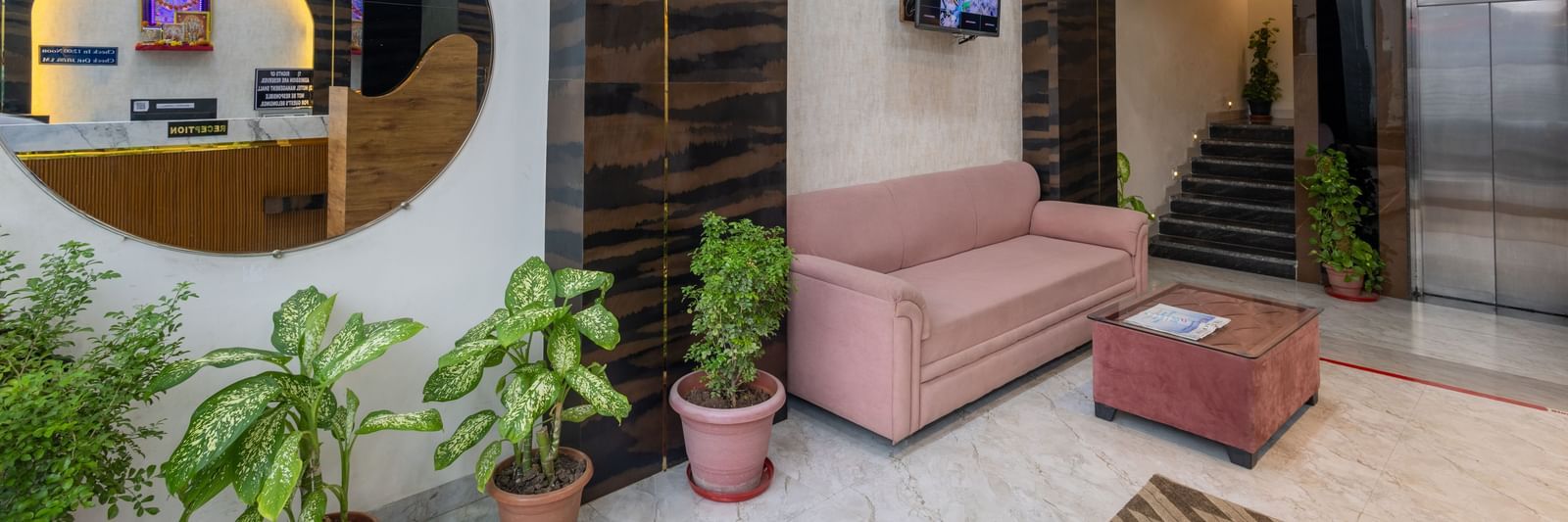 Lobby with round mirror, pink sofa, and potted plants at Pravasa Stay Dewas Naka, Indore.