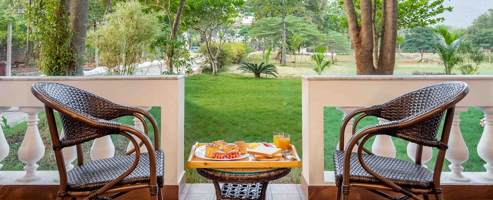A view from a balcony at Avana Resort overlooking a lush green lawn and numerous trees, with mountains visible in the distance.