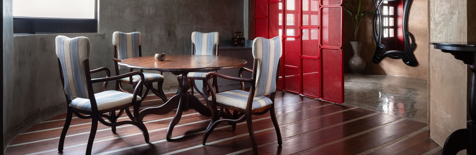 A dining area at Shilton International, Kochi, with a round table, chairs, wooden floor, coffered ceiling, and a partition.