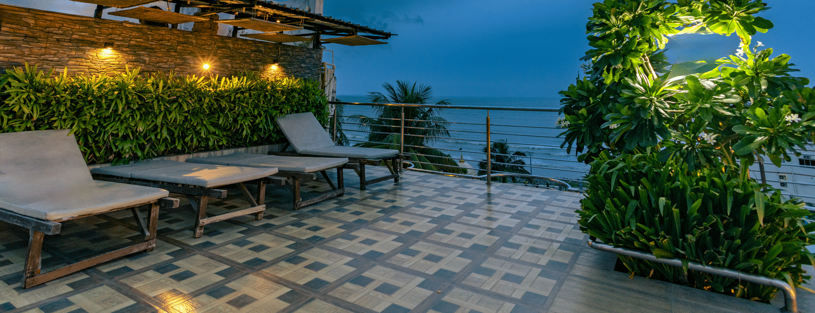 An outdoor seating area with tables, sun loungers, plants and a cloudy sky at Hotel Seagull Digha.