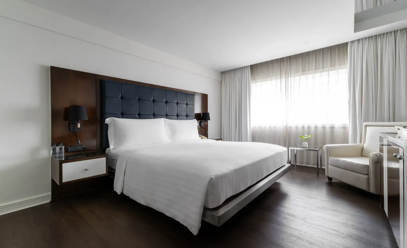 Double bed with dark wooden headboard, integrated lighting, and white bedding at Night Hotel Bangkok.