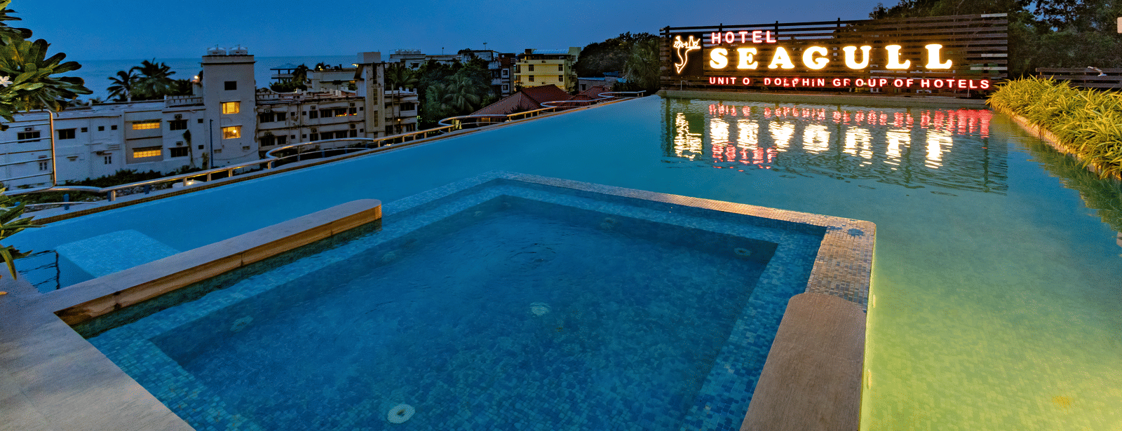 A poolside view with the ‘Seagull’ signage reflected in the swimming pool under a cloudy sky at Hotel Seagull Digha.