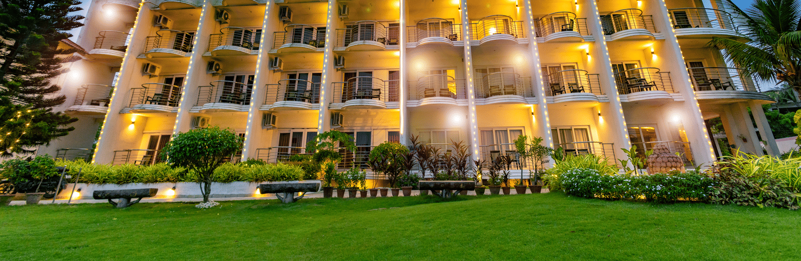 A multi-storey hotel exterior with illuminated windows, and a vibrant green lawn at twilight - Hotel Seagull Digha