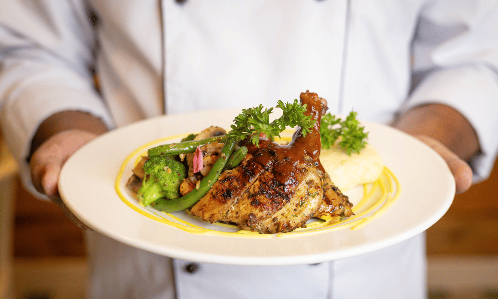 A chef holding a plate of grilled meat served with mashed potatoes and vegetables - Megha Resort & Villas, Dehradun