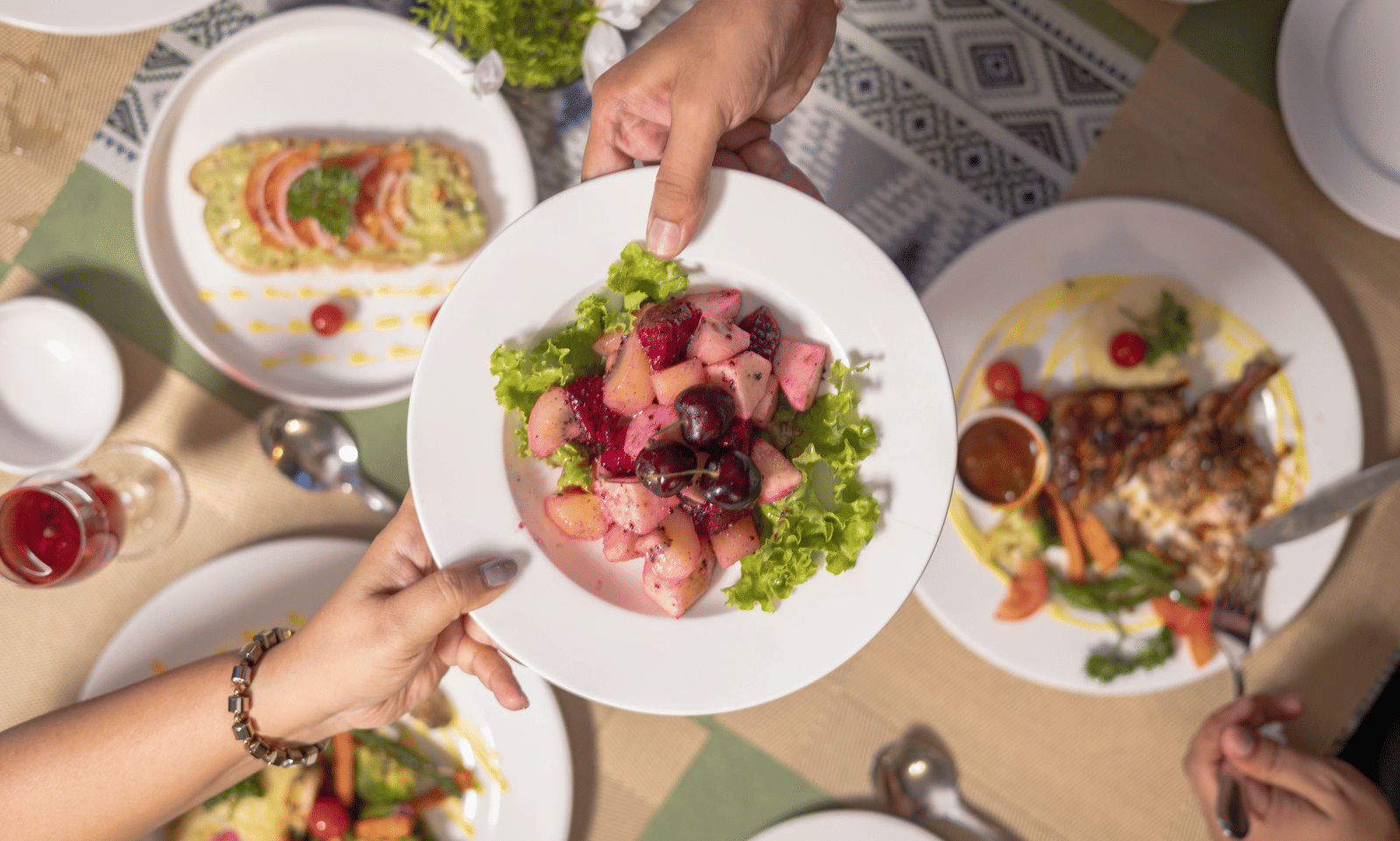 Plates of salad and dishes on a dining table featuring a dish at the middle held by two hands on the either side at Megha Resort & Villas, Dehradun.