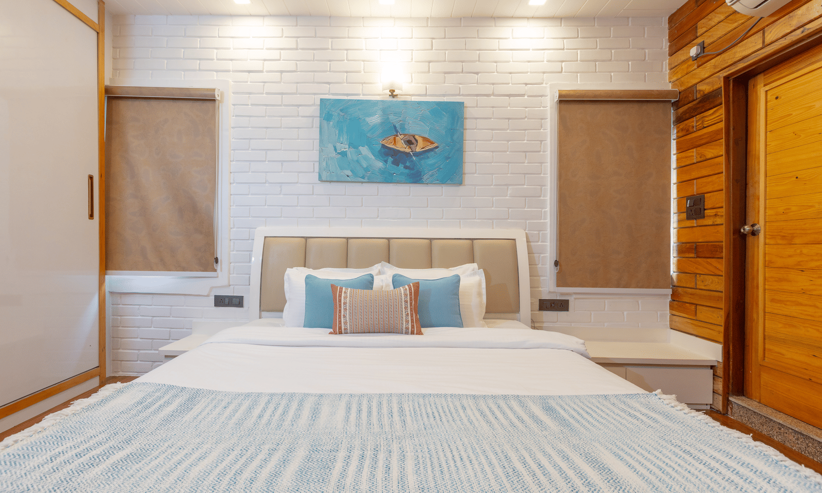 A well-lit bedroom featuring a white brick wall, a king sized bed, and an abstract artwork at Megha Resort & Villas, Dehradun.