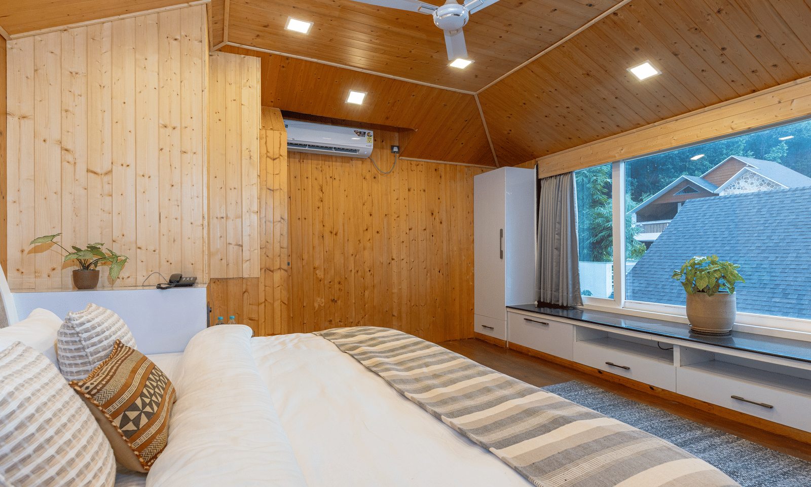 A bright, wood-panelled bedroom with a large bed, wide window, and a light, airy atmosphere at Megha Resort & Villas, Dehradun.