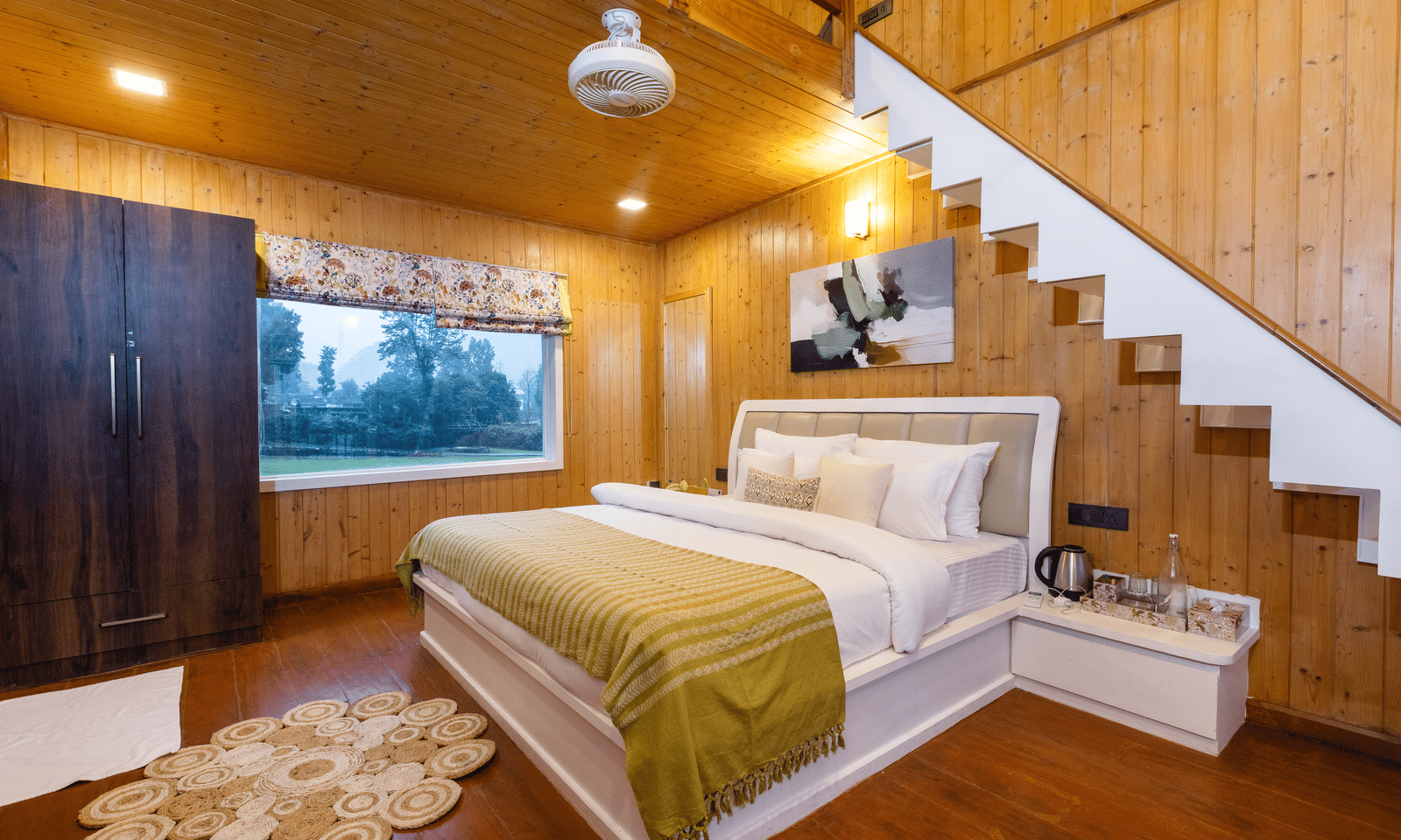 A light, wooden-panelled bedroom featuring a double bed, a wooden wardrobe, and an internal staircase - Megha Resort & Villas, Dehradun