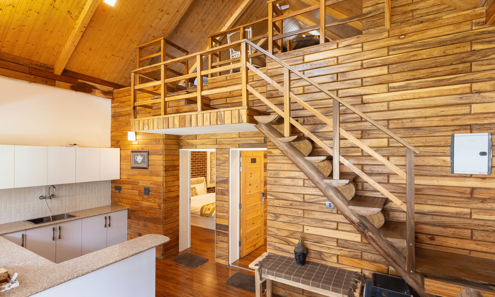 A rustic interior with wooden walls and an open-tread staircase leading up from the kitchen area at Megha Resort & Villas, Dehradun.