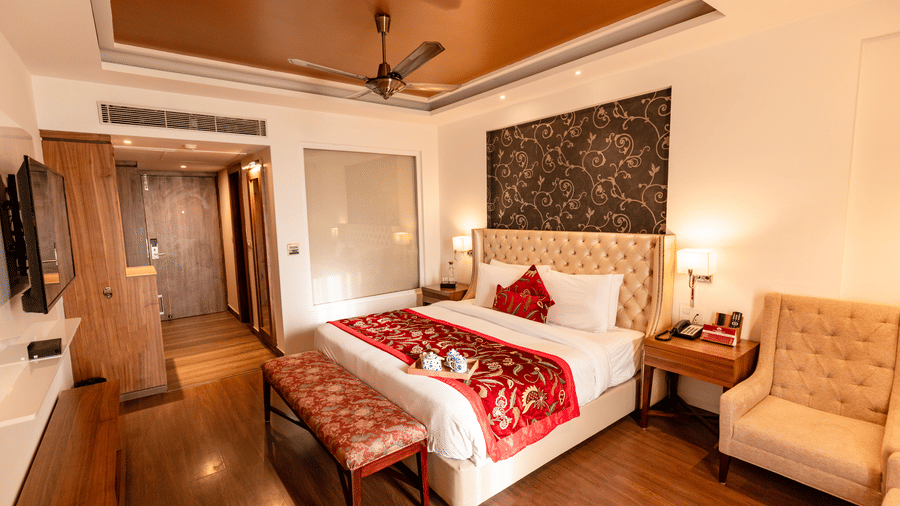 A bedroom with a king size bed, side tables, lamps, wall-mounted TV, armchair, and wardrobe arranged indoors at Indraprastha Resort & Spa, McLeod Ganj.