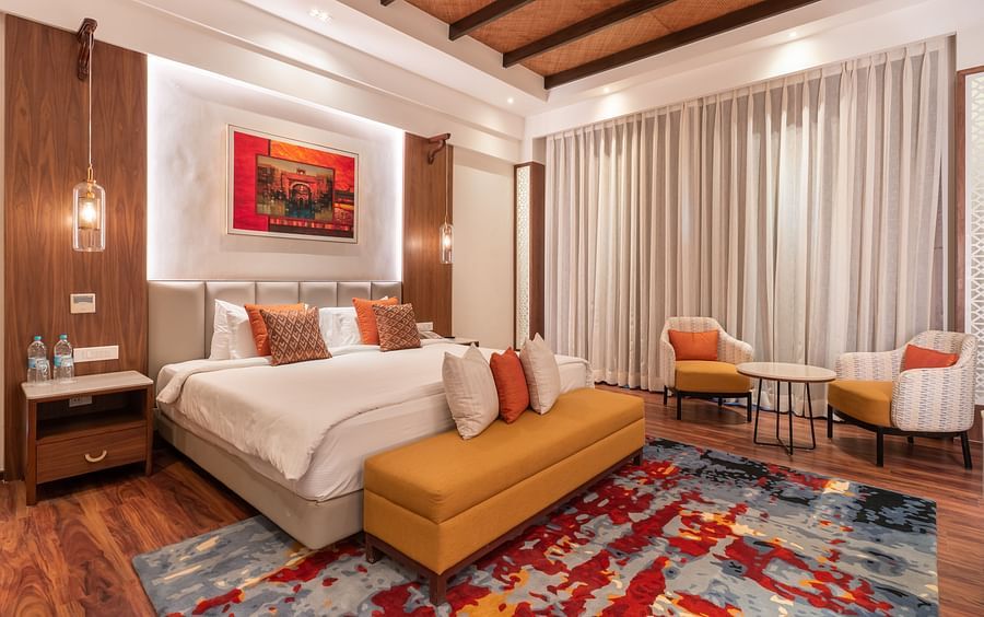 A view of the grand suite room with a bed, ottoman, study table and chairs - The Ananta Udaipur