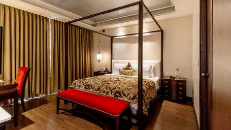 A bedroom with a 4 poster bed, side tables, work desk, and curtains, inside at Indraprastha Resort & Spa, McLeod Ganj.