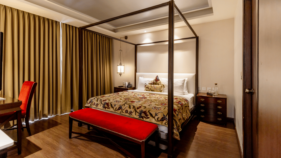 A bedroom with a 4 poster bed, side tables, work desk, and curtains, inside at Indraprastha Resort & Spa, McLeod Ganj.