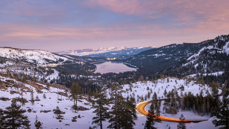 A wide-angle shot of the Carson Pass with the landscape around the lake covered with snow with a beautiful sunset sky with blue and orange hues in the background.