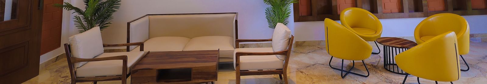 Lounge area with wooden ceiling, green plants, and beige sofa at Trishvam Symphony, Krishnagiri.