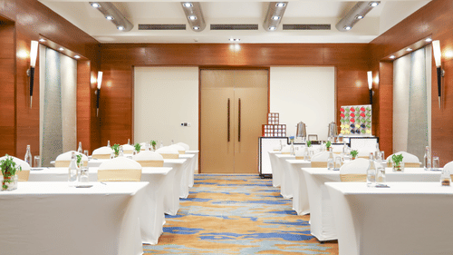 A photo of a conference room with tables covered in white cloths, water bottles, and a refreshment station - Balaji Sarovar Premiere, Solapur
