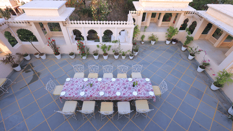 A courtyard view with central dining table setup in open space at Akshay Niwas Boutique Hotel by Amantra, Udaipur, showing surrounding arches and flooring.