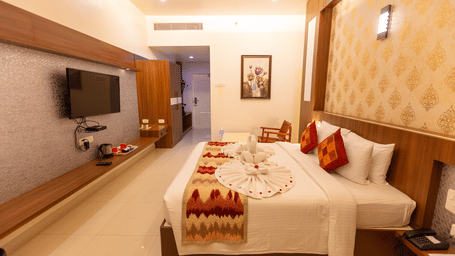 A Royal Executive Room at DSF Grand Plaza, Tuticorin with a king bed dressed with a towel swan, damask wallpaper, a wall-mounted TV, and a wooden rocking chair.