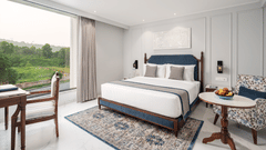 An image of our hotel room in Haridwar featuring a large bed, an upholstered sofa, a round table, and a scenic view - MJ Sarovar Portico, Haridwar