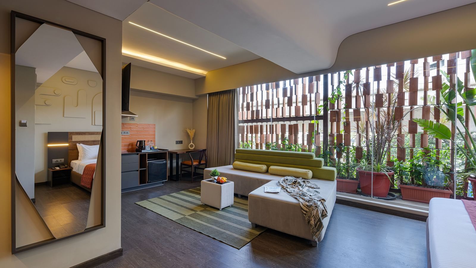 A lounger sofa with with a dining table on one end and open space in the other end, behind it the wall has transparent glass and a lot of plants can be seen through it.
