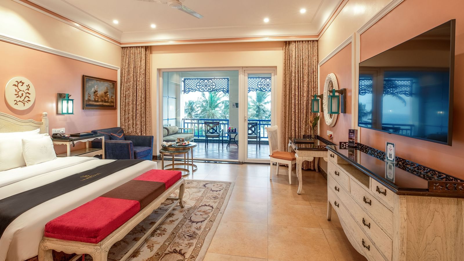 Spacious bedroom with seating area, a workstation, a ceiling fan, a wall-mounted TV, and large glass windows at MAYFAIR Palm Beach Resort, Gopalpur-On-Sea