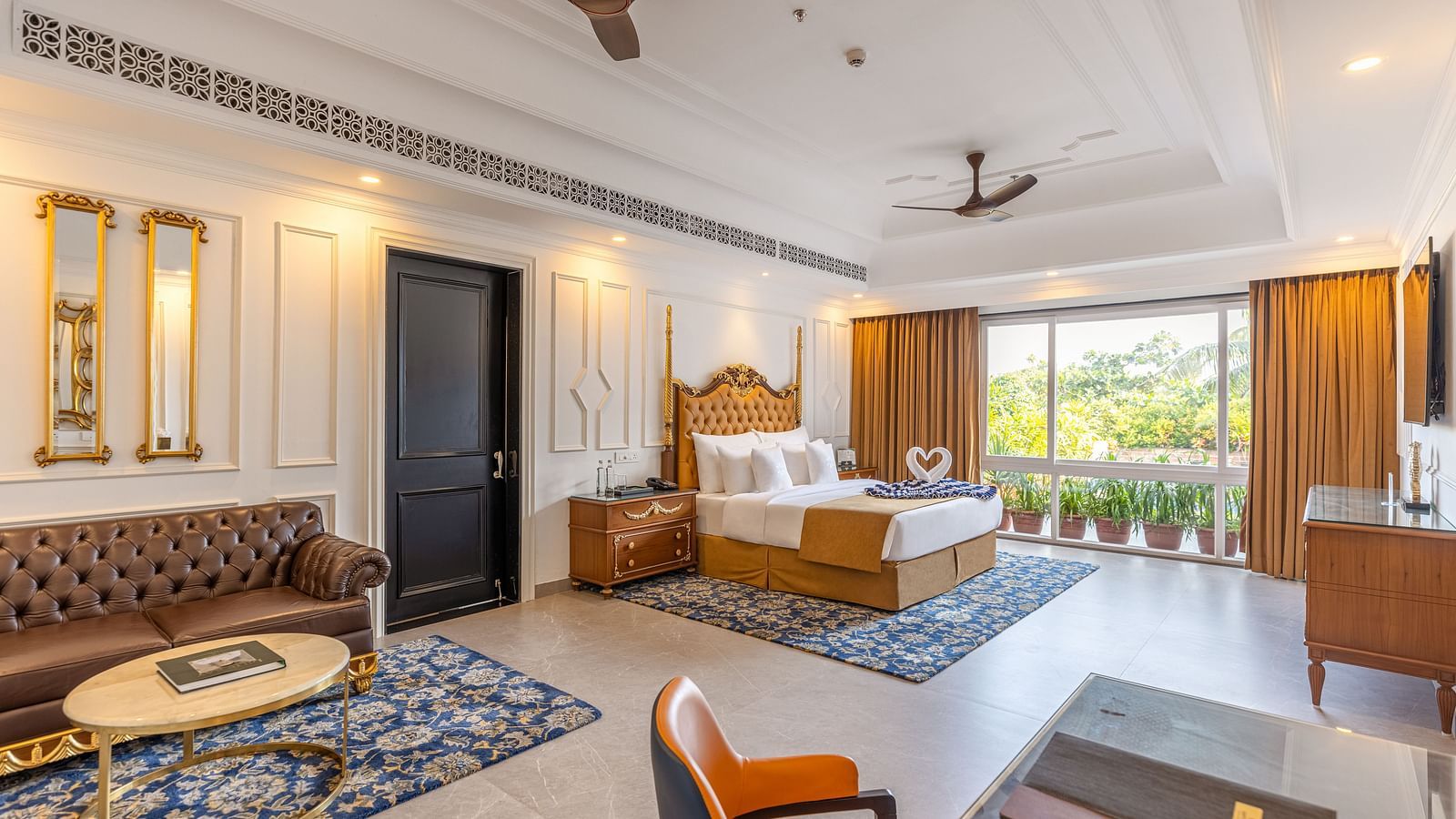 Spacious bedroom with workstation, lounge area, wall-mounted TV, bedside table, two ceiling fans, and large glass windows at MAYFAIR Palm Beach Resort, Gopalpur-On-Sea