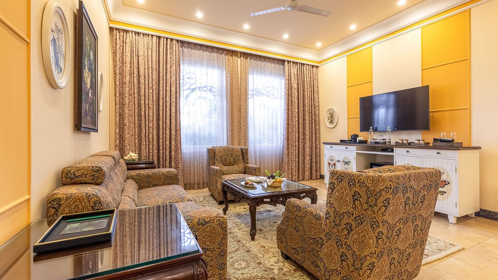 Cozy and well-lit sitting room with patterned armchairs, coffee table, and a large TV unit at MAYFAIR Palm Beach Resort, Gopalpur-On-Sea.