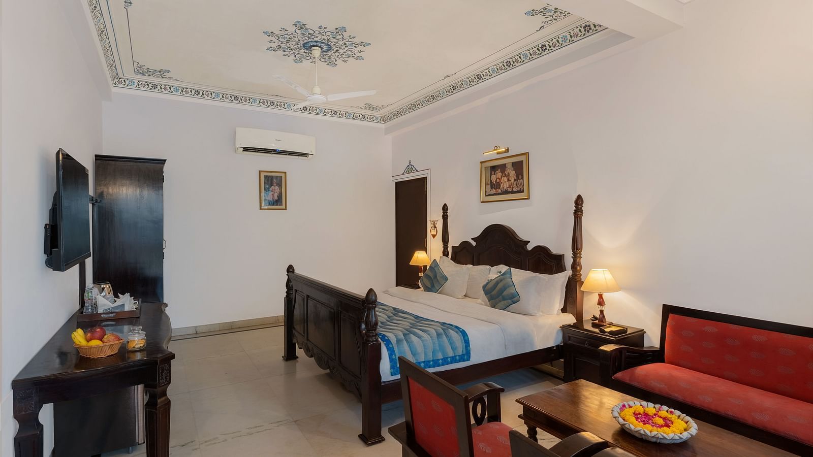 A spacious bedroom featuring a wooden table, cushioned furniture, and warm lighting | Panna Vilas Udaipur