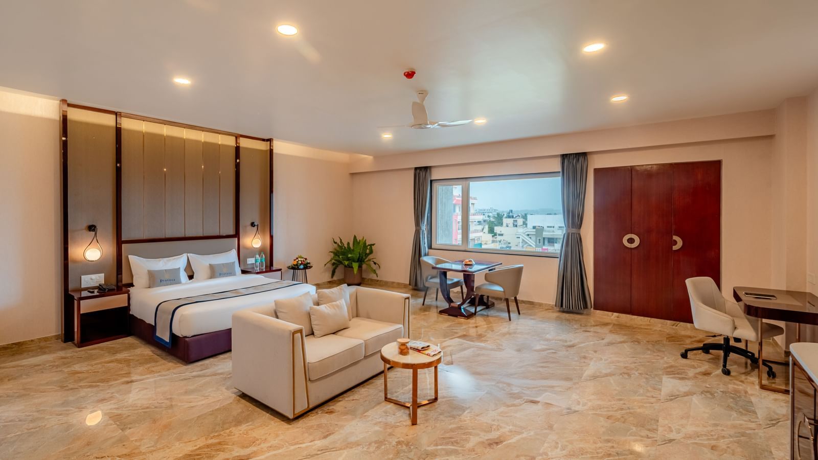 Spacious suite featuring a comfortable bed, a work desk, and city views | Suite | Pravasa Hotel, Vijayapura