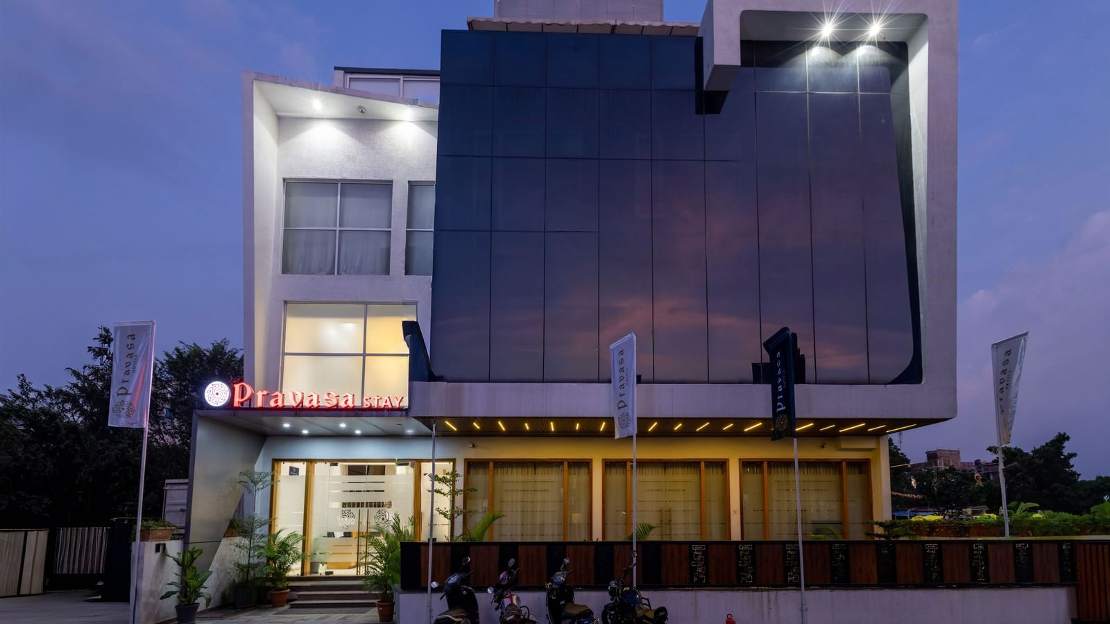 Facade of the well-lit Pravasa Stay Vijay Nagar, Indore, as seen under a dark sky.