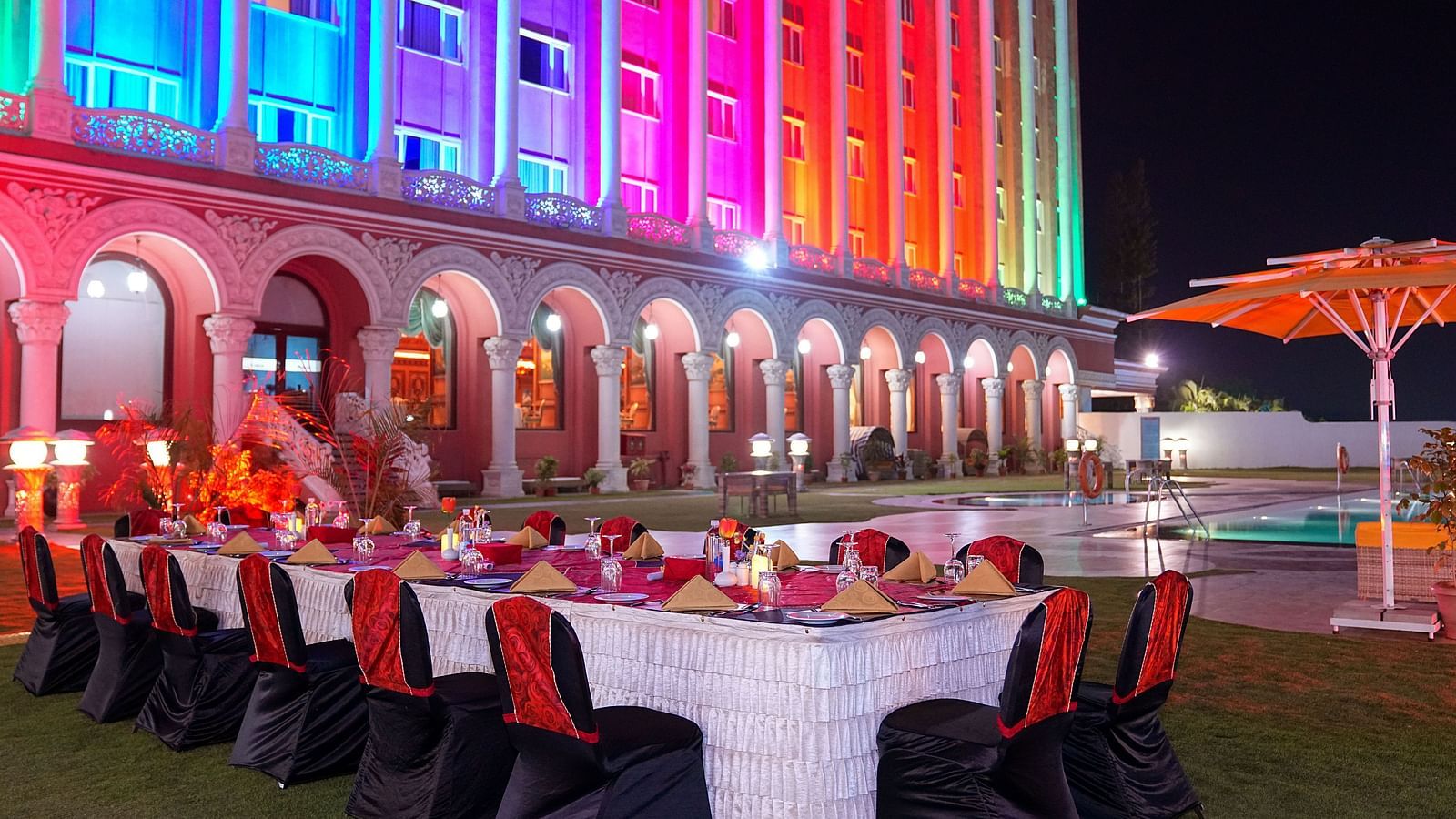 a long banquet table with plates and candles on top of it with Sitara Luxury Hotel in the background - Ramoji Film City Hotels - Hyderabad 