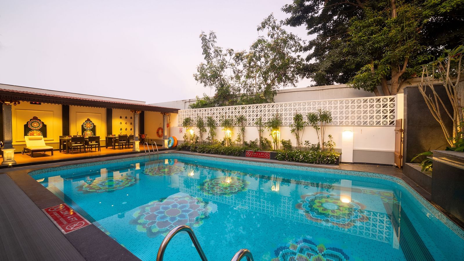 Bright blue pool surrounded by greenery and elegant deck seating. Regency Madurai by GRT Hotels