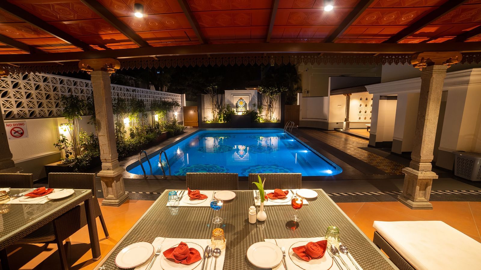 Poolside dining with a warm evening ambiance under a red canopy. Regency Madurai by GRT Hotels