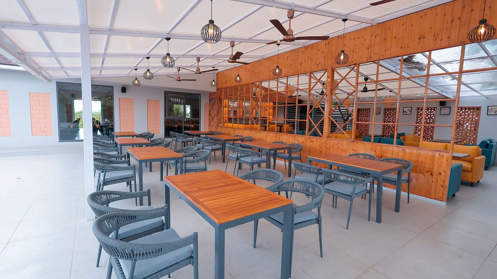 Indoor dining area at Trishvam Symphony, Krishnagiri, with wooden tables, grey chairs, and a bright semi-open layout.