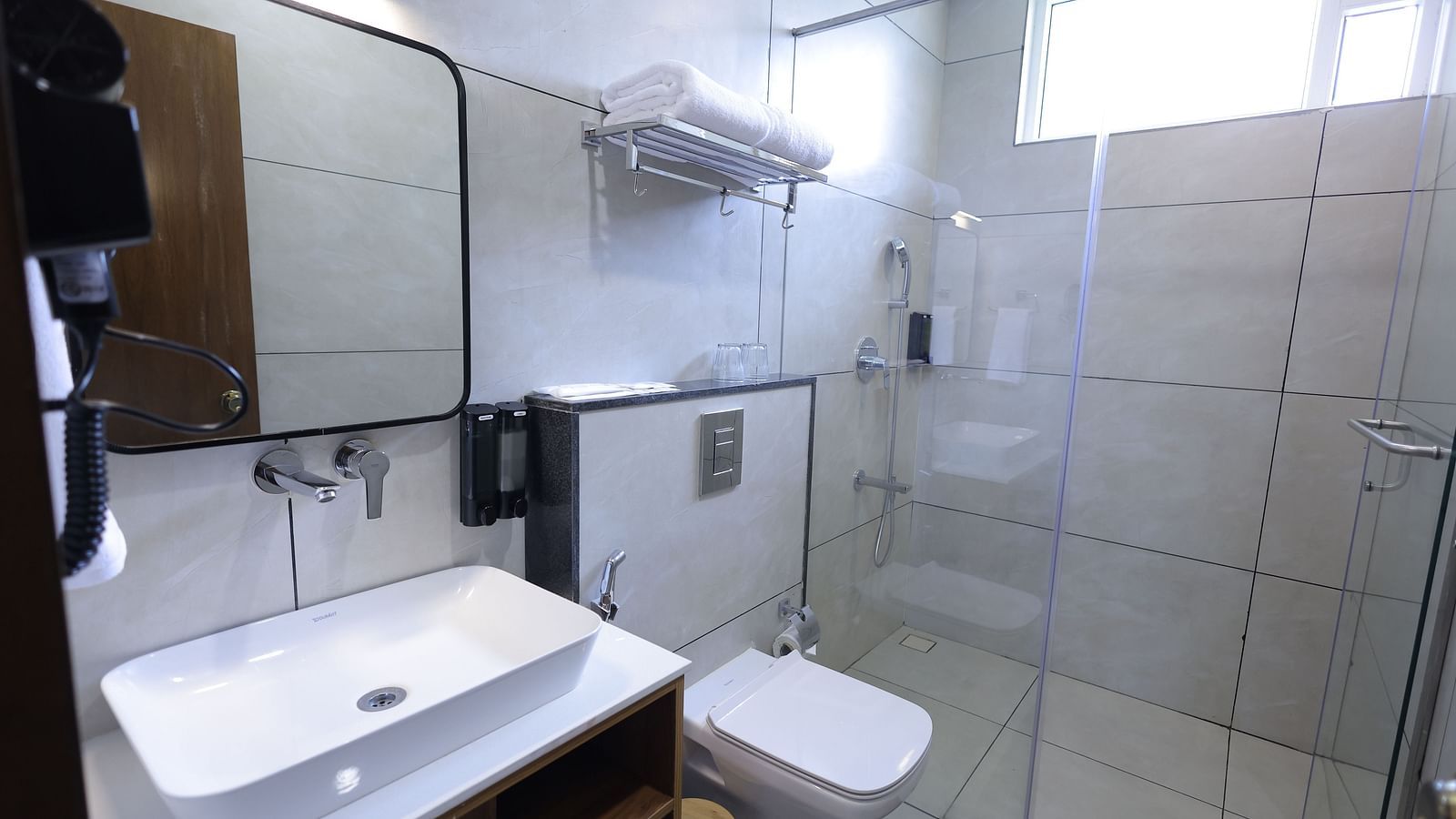 Bathroom with glass shower, mirror, and sink area at Trishvam Symphony, Krishnagiri.