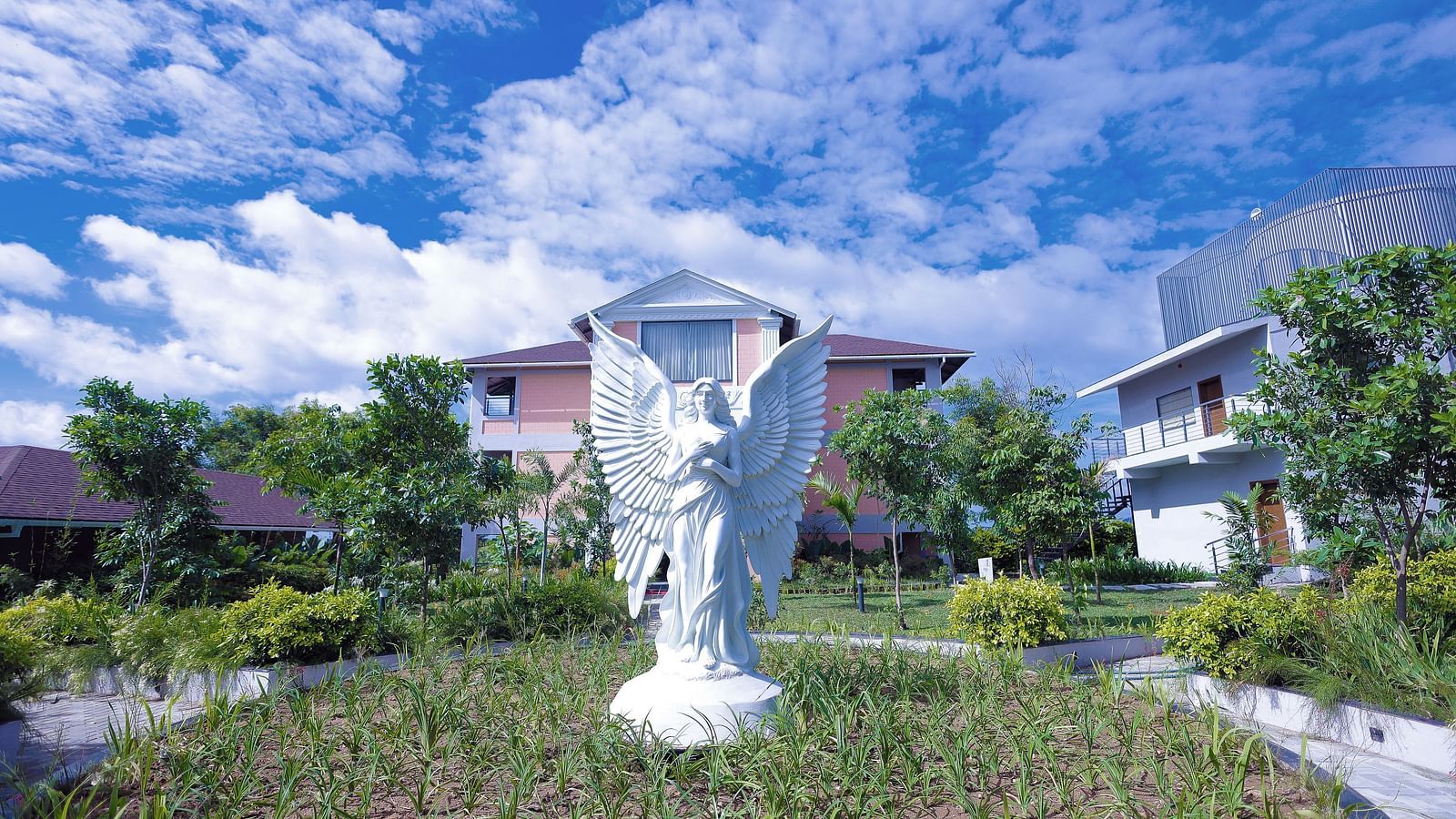 White angel sculpture in landscaped garden with villas in the background at Trishvam Symphony, Krishnagiri.