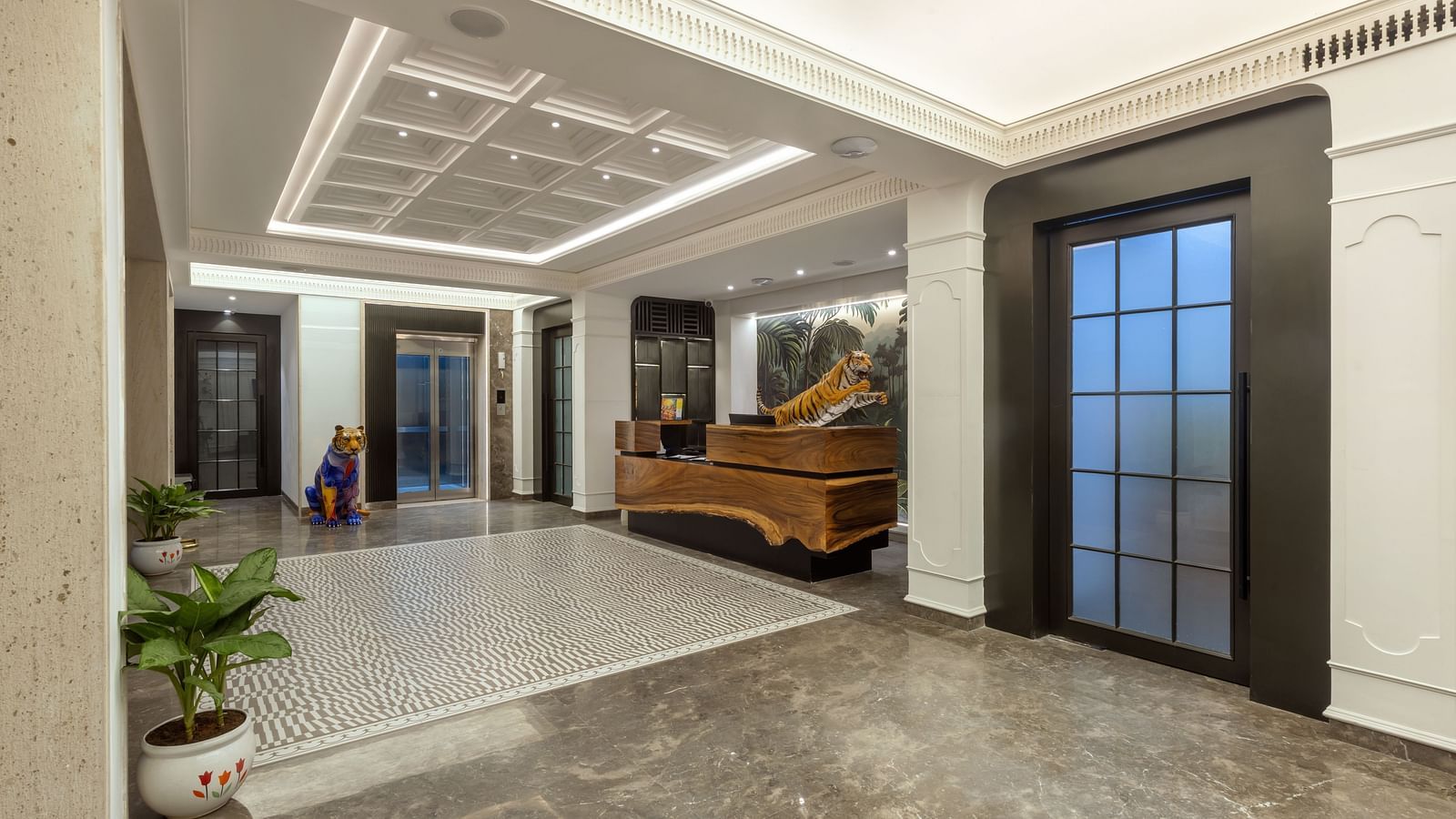 Lobby view at Zibe Luxe Hyderabad by GRT Hotels showcasing the reception area, modern lighting, elevator, and a colorful tiger sculpture.