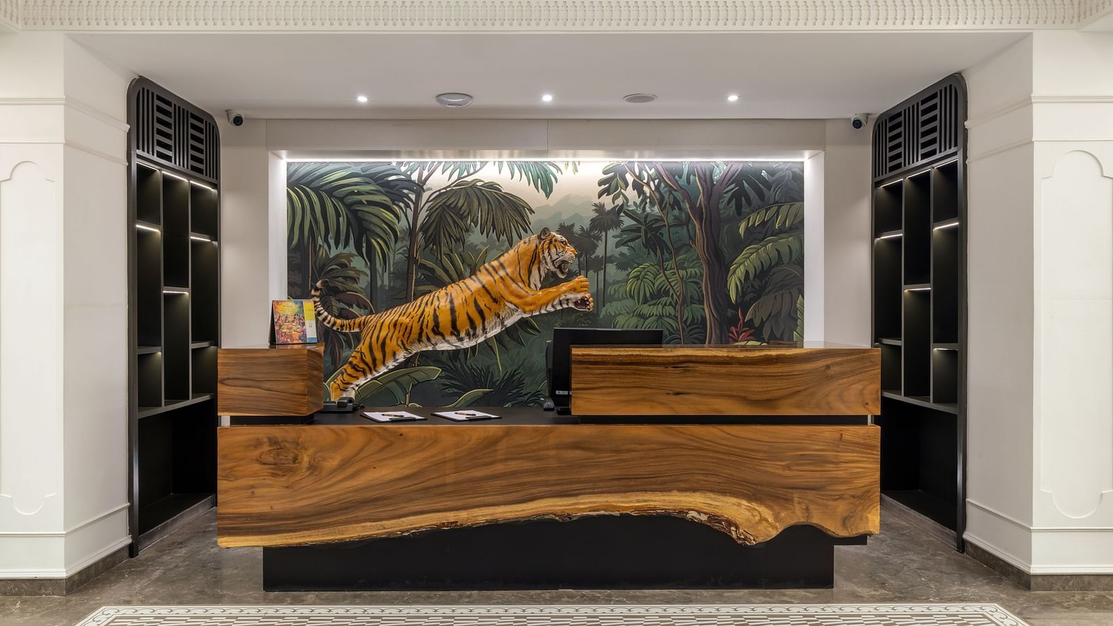 Front desk at Zibe Luxe Hyderabad by GRT Hotels featuring a sculpted wooden counter and a vibrant jungle mural with a leaping tiger.