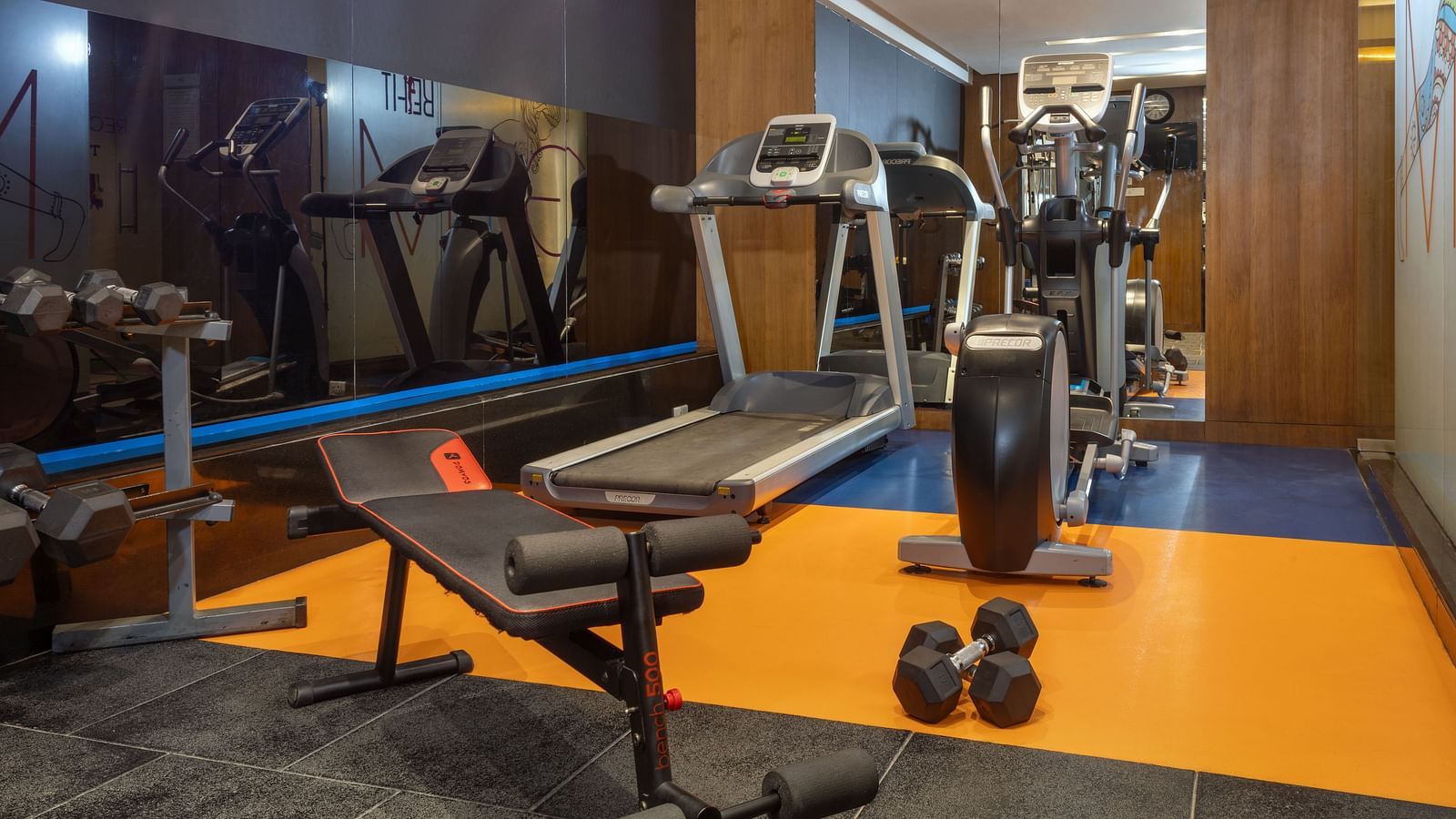 Fitness centre at Zibe Luxe Hyderabad by GRT Hotels featuring treadmills, elliptical machines, weights, and energetic flooring design.
