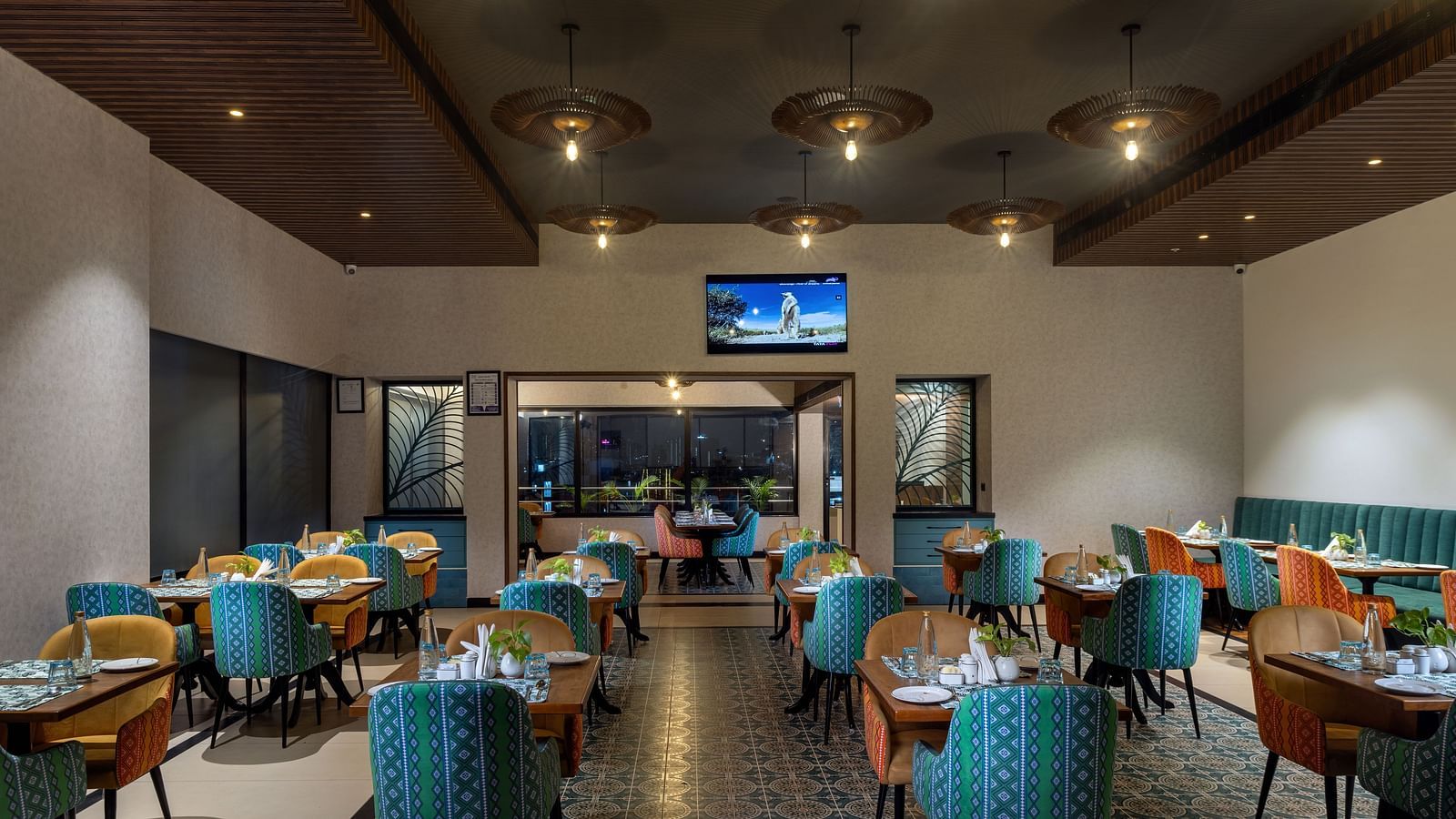 Cosy indoor dining at Shalimar Restaurant in Zibe Luxe Hyderabad by GRT Hotels, with patterned flooring, a central TV, and ambient lighting.