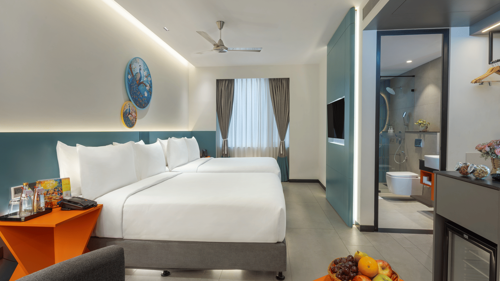 One of Zibe's hotel room in JP Nagar, Hyderabad, featuring twin beds, an attached washroom, a wall-mounted television, and a night stand.