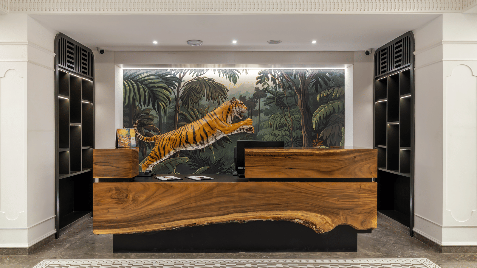 Front desk at best hotel in Kukatpally featuring a sculpted wooden counter and a vibrant jungle mural with a leaping tiger | Zibe Luxe Hyderabad by GRT Hotels