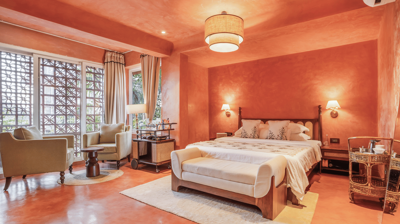 Inviting bedroom at Unseen Boutique Hotel with orange walls, soft lighting, and large windows enhancing a warm, uplifting ambience.