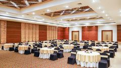 Spacious conference hall featuring round tables with black chair covers and floral centrepieces, set up for an event - Balaji Sarovar Premiere, Solapur
