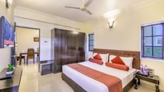 a hotel room in Candolim featuring a double bed with orange bed runner, a wooden wardrobe, a wall-mounted television and ambient lighting - Golden Tulip, Candolim, Goa