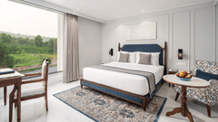 An image of our hotel room in Haridwar featuring a large bed, an upholstered sofa, a round table, and a scenic view - MJ Sarovar Portico, Haridwar