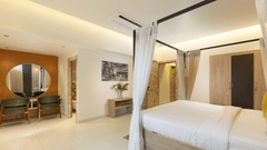 A luxurious hotel bedroom featuring a four-poster bed with white drapes, a vanity table with a mirror, and an armchair - Pride Premier Dehradun
